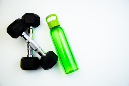 Dumbbells and a green water bottle are arranged on a white background, representing fitness and hydration, ideal for promoting health and wellness activitiesの写真素材