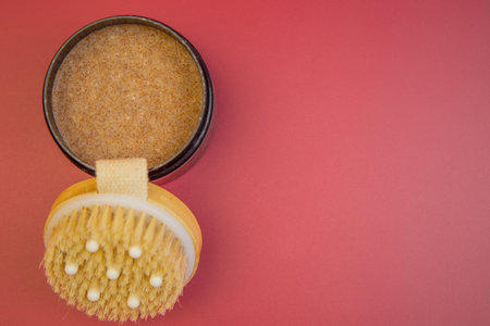 Spa essentials include a round jar filled with brown sugar scrub and a natural bristle body brush on a vibrant pink background, ideal for wellness and relaxation themesの写真素材