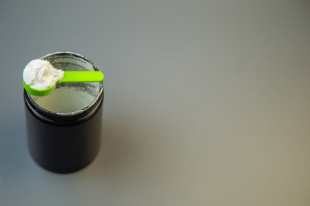 Black jar filled with white powder and green scoop on gray surface, representing nutritional...