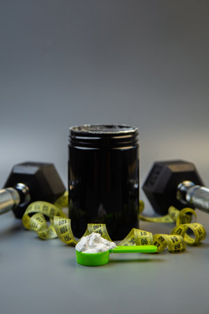 Fitness supplement jar with green scoop and protein powder, accompanied by dumbbells and measuring tape, illustrating a commitment to health and fitness goalsの写真素材