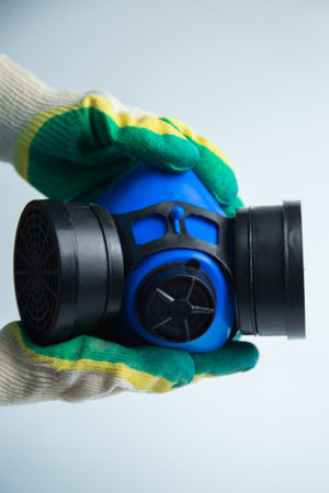 Close-up of hands in construction gloves holding a protective blue mask with two filters on the sides on a white background. Concept of personal protective equipment, respiratory protection, repair. High quality photo