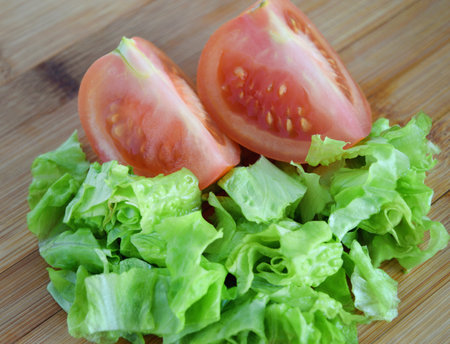 Two slices of red tomato and green lettuce on wooden background.の写真素材