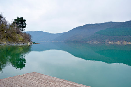 Beautiful reflection of forest mountains in a green lake in cloudy weatherの写真素材
