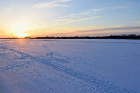 A beautiful winter sunset over a frozen river covered with white snow and footprints on itの写真素材