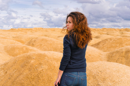 A young woman with red hair stands with her back to the camera in a desert with sand dunes of bizarre shapeの写真素材