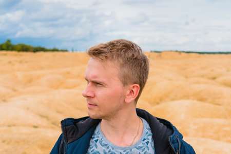 Portrait of a young blond man in a jacket on in the desert with sand dunes of bizarre shapeの写真素材