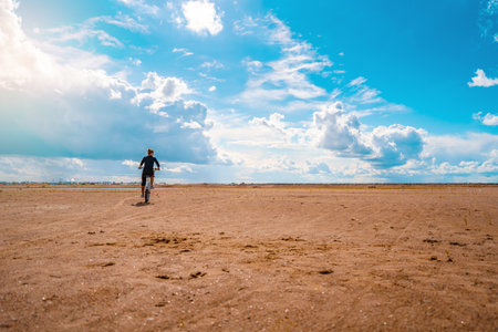 A woman on a Bicycle rides on the sand on a Sunny day, leaving footprints in the sandの写真素材