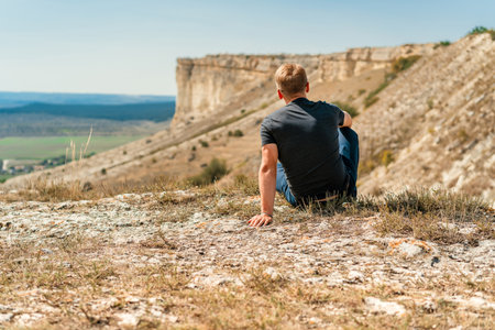 Handsome young blond man sitting on a cliff overlooking the rustic landscape, White rock in Crimeaの写真素材