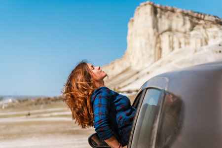 A young happy girl leans out of a car window on a trip to Crimea against a White rock background, concept of freedomの写真素材