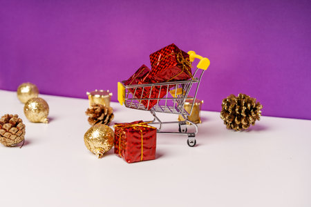 The concept of new year's holiday sales. Mini cart with gifts on a purple background with scattered Christmas decorations aroundの写真素材