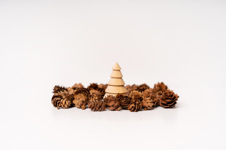 A wooden model of a Christmas tree stands surrounded by cones on a white background. Christmas...