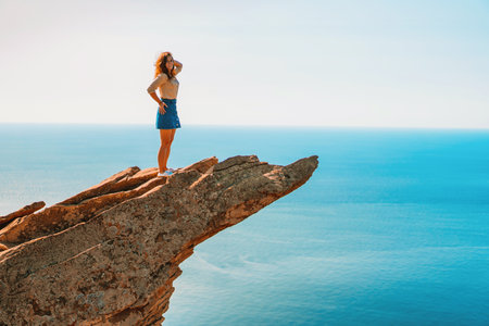 A young woman stands on a picturesque rock ledge above the sea against the sky. The concept of travel and freedom.の写真素材