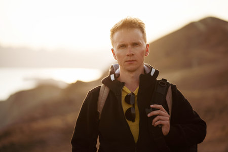 Picturesque mountain landscape at sunset with the sea on the horizon, a young blond man with...