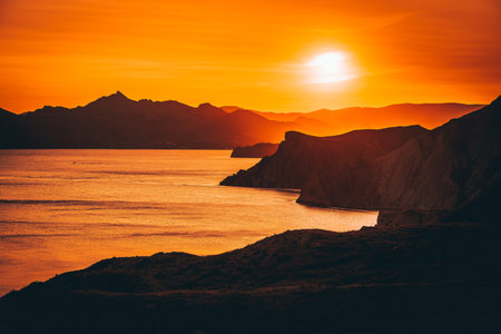 Hilly landscape by the sea in a bright orange sunset. Layers of mountains at sunset, background imageの写真素材