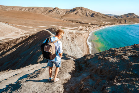 A man in a white shirt stands on the slope of Cape chameleon with an amazing panoramic view of the hills and the sea from aboveの写真素材