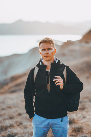 Picturesque mountain landscape at sunset with the sea on the horizon, a young blond man with...