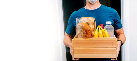 A male courier in a protective mask delivers a box of groceries. Service delivery in terms of quarantine, the concept of self-isolationの写真素材