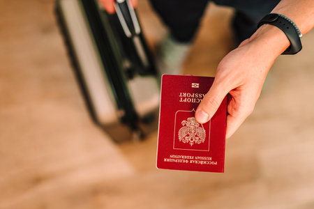A man holds out a Russian passport and holds a suitcase for travel with the other hand, photo aboveの写真素材