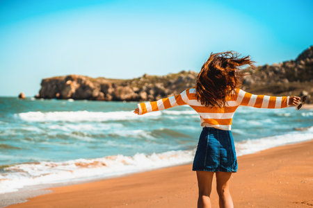 A woman with long hair and a bright yellow sweater walks along the sea on the beach in the cold seasonの写真素材