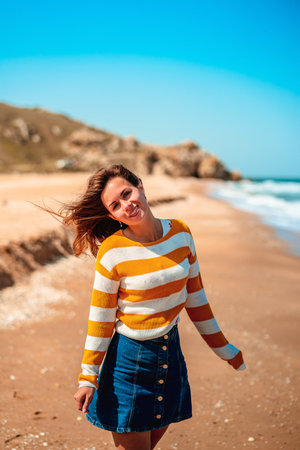 A woman with long hair and a bright yellow sweater walks along the sea on the beach in the cold seasonの写真素材