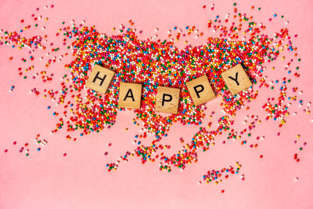 Word HAPPY written on wooden cubes in the middle of colorful confetti on a pink background. The concept of a festive moodの写真素材