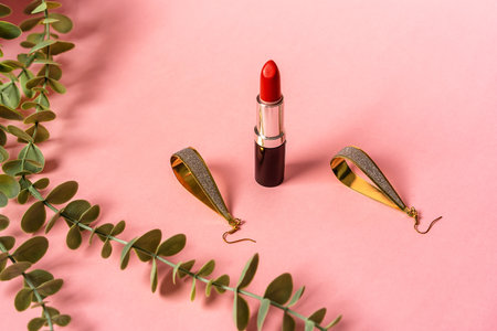 Red lipstick and earrings lie on a pink background next to a lady's bag. Beautiful still life for a fashionable womanの写真素材
