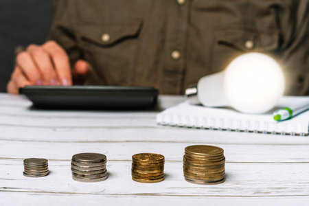 Business man hand holding a light bulb using a calculator to calculate cash flow. The idea of saving energy and accounting Finance in the office conceptの写真素材