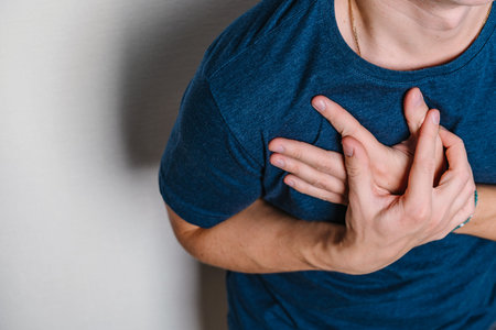 The man feels pain in the area of the heart and holds his chest with two hands. The concept of reflux disease or diseases of the heart system. Space for text on a white backgroundの写真素材