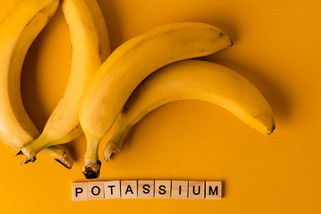 The word "Potassium" is laid out of wooden blocks in the middle of bananas on a yellow background. The concept of a healthy lifestyleの写真素材