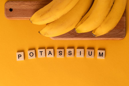 The word "Potassium" is laid out of wooden blocks in the middle of bananas on a yellow background. The concept of a healthy lifestyleの写真素材