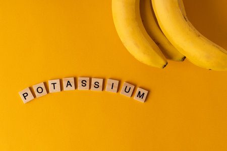 The word "Potassium" is laid out of wooden blocks in the middle of bananas on a yellow background. The concept of a healthy lifestyleの写真素材