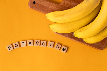 The word "Potassium" is laid out of wooden blocks in the middle of bananas on a yellow background. The concept of a healthy lifestyleの写真素材