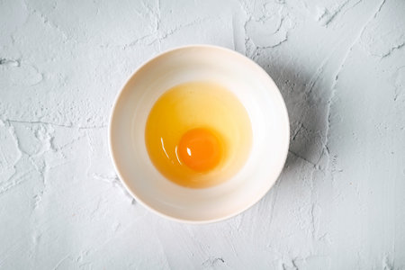 Egg and yolk in a bowl on a white marble table. Minimalist concept of cooking
