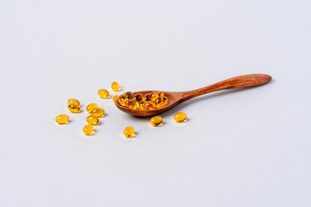 Yellow capsules of vitamin D or fish oil on a wooden spoonの写真素材