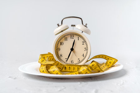 Sports and weight loss concept. The alarm clock is wrapped with measuring tape and dumbbells on a...