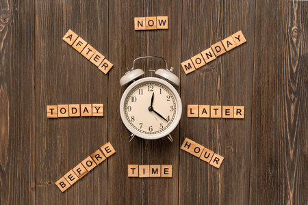 The alarm clock is on a wooden table and words made of wooden blocks are around it. Planning and...