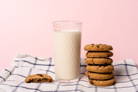 oatmeal chocolate chip cookies and a glass of milk on a checkered towel on a pastel pink background...