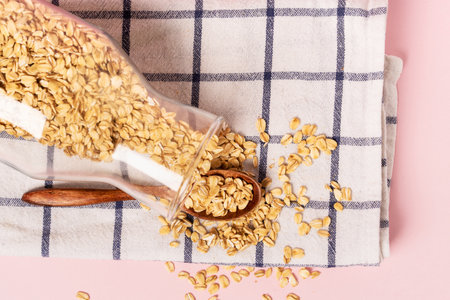 Glass jar with dry oatmeal on a checkered kitchen towel, top view