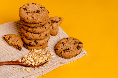 Oatmeal chocolate chip cookies on a kitchen towel on a yellow background with space for textの写真素材