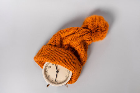 Round alarm clock in a knitted warm green hat on the background. The concept of the winter season. Space for textの写真素材
