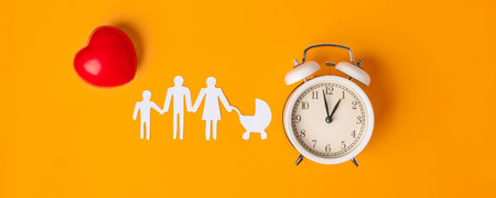 White paper family with parents and children, alarm clock as a reminder symbol to give birth to another child, on a yellow backgroundの写真素材