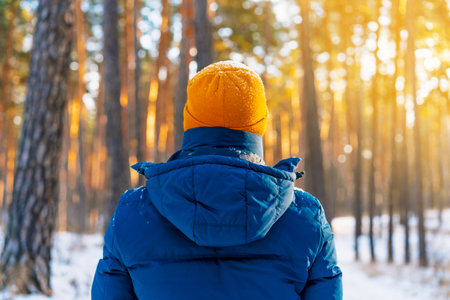 Rear view of man in a winter jacket stands against the background of a frozen river with a winter landscapeの写真素材