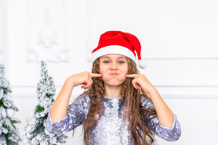 Cute little girl smiles and looks at the camera in a bright studio with Christmas decorationsの写真素材
