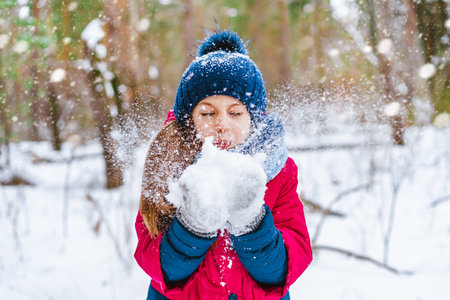 Rear view of a little girl in a red jacket standing in the middle of a path in a winter pine forestの写真素材