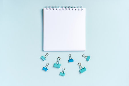 An empty blank notepad for writing on a blue background and paper clips and clips around itの写真素材