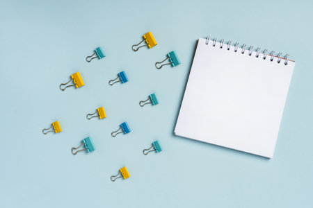 An empty blank notepad for writing on a blue background and paper clips and clips around it