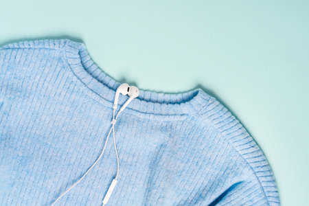 White headphones lie on a blue knitted sweater on a pastel backgroundの写真素材