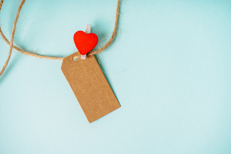 Craft tag with a place for text and a clothespin in the form of a heart on a blue background. Greeting card concept for loved onesの写真素材