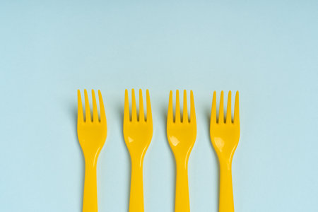 Yellow plastic disposable forks arranged in a row on a blue background, minimalism. The concept of pollution of the environmentの写真素材