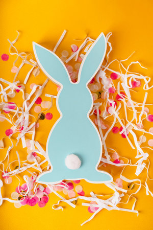 Easter wooden rabbit with colored confetti on yellow backgroundの写真素材